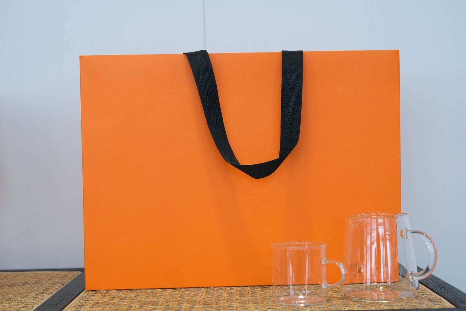 Large orange paper bag sample with black flat ribbon handles shown beside glassware for scale